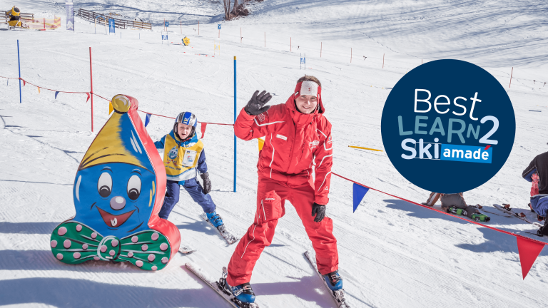 Skilehrer mit Kind im Schnee neben einem bunten Schneemann bei der Skischule Dorfgastein.